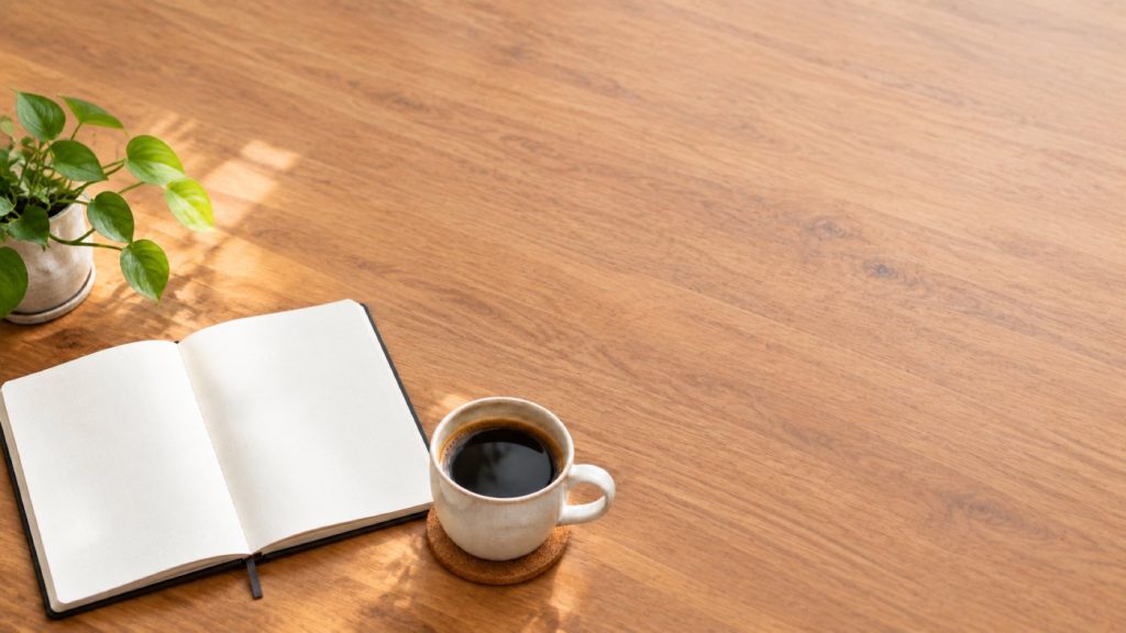 The same desk recomposed so the notebook and cup sit in the lower left and the top right of the frame is empty.