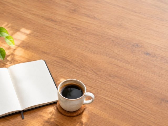 The same desk recomposed so the notebook and cup sit in the lower left and the top right of the frame is empty.